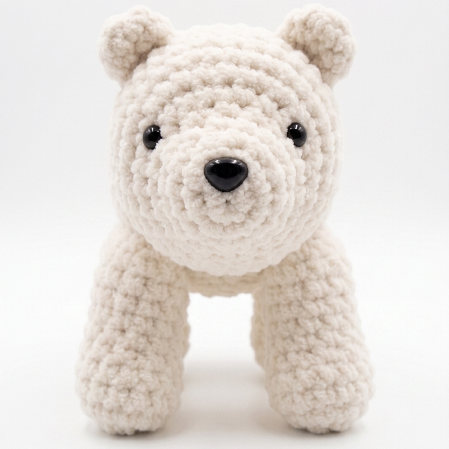 A small crocheted polar bear toy in a soft off-white or cream yarn, featuring black bead eyes and a black nose, set against a seamless white studio background.