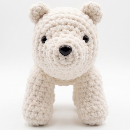 A small crocheted polar bear toy in a soft off-white or cream yarn, featuring black bead eyes and a black nose, set against a seamless white studio background.