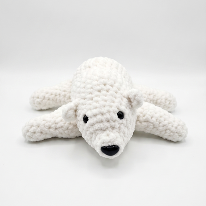 A white crocheted polar bear toy with black embroidered eyes and nose, lying on a light gray studio background.