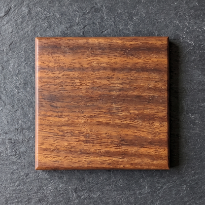 A square African Walnut coaster with a hardwax oil finish, centered on a dark gray slate background